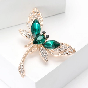 Detailed close-up of a gold dragonfly brooch with green crystals and white rhinestones