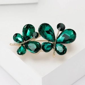 Élégante broche papillon dorée avec cristaux vert émeraude sur socle blanc moderne