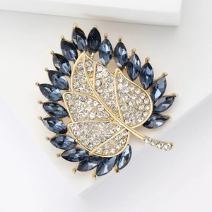 Detailaufnahme der Blattbrosche mit blauen Kristallen und klaren Strasssteinen in Gold