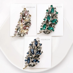 Detailed close-up of leaf-shaped rhinestone brooches in pink, emerald, and dark blue colors