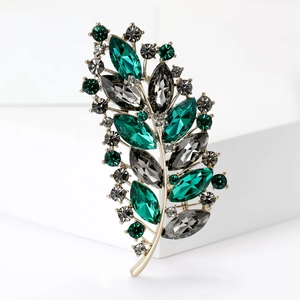 Close-up of luxury leaf brooch with emerald green and dark grey rhinestones on gold base