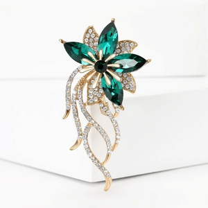 Dettaglio di elegante spilla a fiore dorato con petali verde smeraldo e nappe di cristallo
