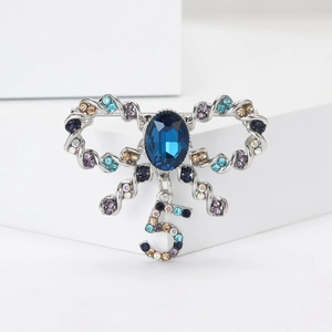 Macro detail of silver bow brooch with blue oval gemstone and number 5 rhinestone pendant