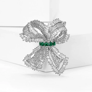 Macro shot of silver bow brooch featuring micro-pave white zircons and emerald accents
