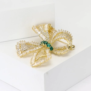 Luxurious gold bow brooch with micro-paved white zircons and a green gemstone center