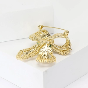 Macro detail of a gold bow brooch with sparkling green crystals and secure pin clasp