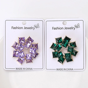 Detail of round gold brooch with square purple and green crystals on display card
