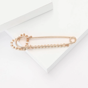 Détail d'une broche double cœur en or rose avec texture perlée sur des blocs blancs