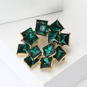 Macro shot of emerald green square-cut gemstones on a luxury golden circular brooch