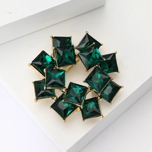 Close-up of vintage gold brooch with emerald-green square crystals in a layered design