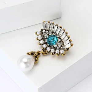 Broche œil maléfique de luxe avec cristal bleu, strass et perle sur bloc blanc