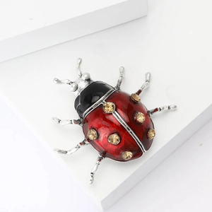 Broche coccinelle en émail rouge et strass dorés sur un support géométrique blanc