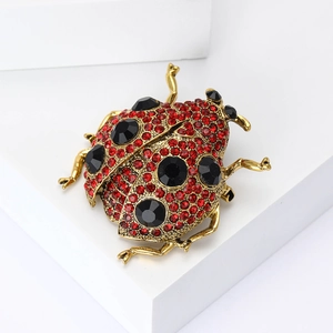 Broche coccinelle dorée raffinée ornée de strass rouges et pierres noires sur fond blanc