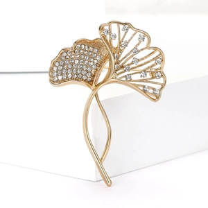 Elegant gold ginkgo leaf brooch with sparkling crystals on minimalist white pedestals