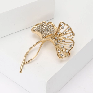 Elegant gold ginkgo leaf brooch with sparkling crystals on a minimalist white stand