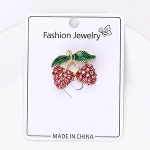 Dettaglio spilla a fragola con strass rosa e foglia smaltata su cartoncino bianco