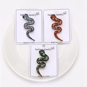 Détail de broches serpent évidées avec strass colorés présentées sur carte support