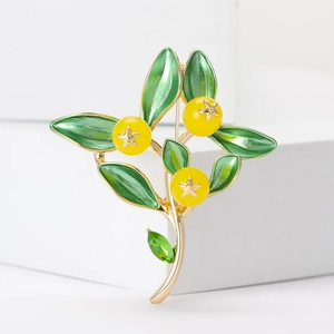 Détail d'une élégante broche dorée avec feuilles en émail vert et fruits jaunes