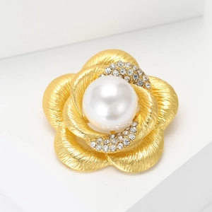 Élégante broche fleur camélia en or mat avec perle et cristaux sur un fond blanc épuré