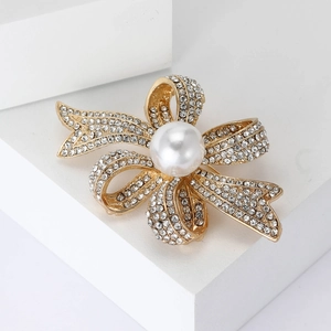 Broche nœud élégante en métal doré avec strass brillants et perle sur fond blanc