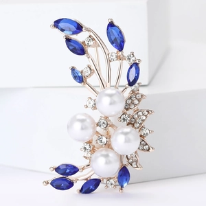 Detailed macro view of rose gold floral brooch with blue gems, pearls, and crystals