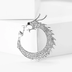 Macro detail of silver Chinese dragon brooch with clear rhinestones on white cube pedestal