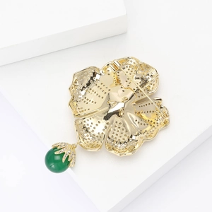 Macro detail of golden flower brooch back with pin clasp and green gemstone pendant