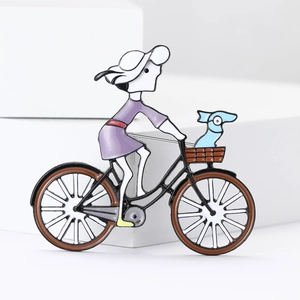 Dettaglio di una spilla con ragazza in bici, cappello bianco e vestito viola su base