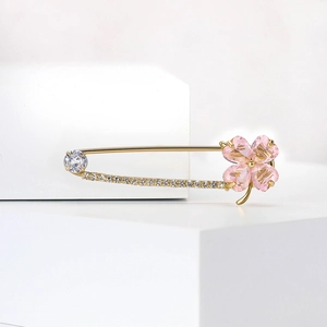 Détail de la broche trèfle doré avec cristaux roses et strass blancs sur fond épuré