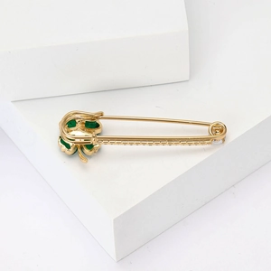 Détail d'une broche en forme d'épingle dorée avec trèfle vert et pierres de zircon blanc