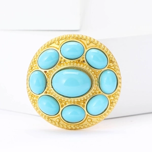 Detail of round gold brooch with oval turquoise stones on white geometric stand