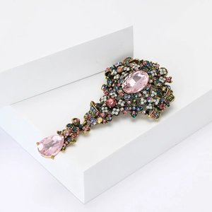 Dettaglio di una spilla vintage in lega con ciondolo rosa e strass colorati brillanti