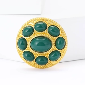 Detail view of a vintage round rhinestone brooch with gold finish and green resin gems