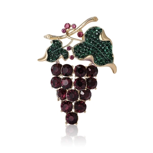 Elegante spilla a grappolo dorata con cristalli viola e strass verdi su sfondo bianco