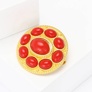 Vintage style gold round brooch with polished red resin stones on a white background