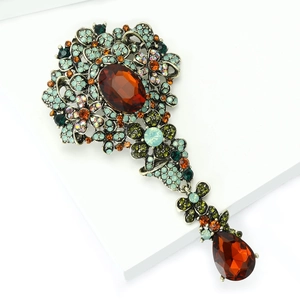 Dettaglio macro di spilla floreale vintage con strass arancione e pendente a goccia