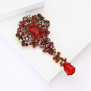 Dettaglio di spilla vintage dorata con strass rossi e motivi floreali traforati