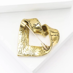 Macro detail of a heart-shaped tape measure brooch in antique gold finish with engravings