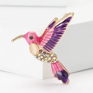 Dettaglio macro della spilla a colibrì con ali in smalto rosa e opale su base bianca