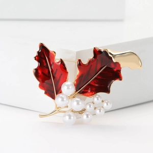 Détail de broche houx avec émail rouge et perles blanches sur monture en métal doré