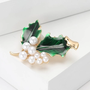 Élégante broche feuille de houx dorée avec émail vert et perles sur support blanc pur