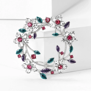 Macro shot of silver rhinestone floral wreath brooch with colorful stones on white podium