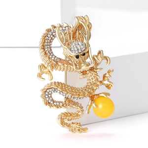 Golden dragon brooch with white crystals and a yellow bead on minimalist white props
