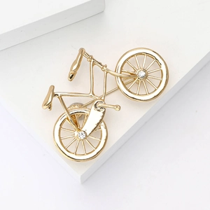 Elegant gold bicycle brooch with white rhinestones on minimalist white display stand