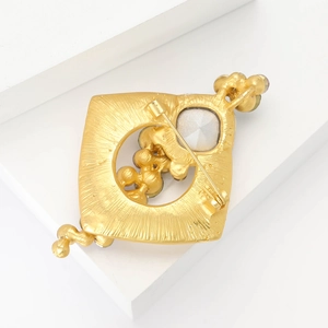 Vue macro d'une broche carrée en or mat avec des détails de cristaux sertis à griffes