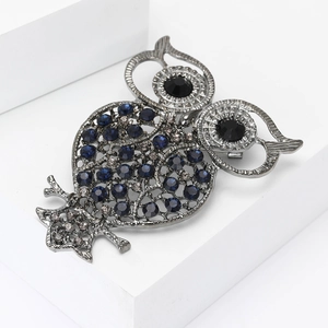 Vintage hollow owl brooch with dark blue rhinestones on a white geometric stand