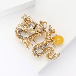Elegant gold plated dragon brooch with sparkling white crystals and a yellow bead on white
