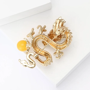 Close-up of golden dragon brooch with yellow bead and intricate metallic scale detail