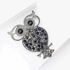 Vintage owl brooch with blue rhinestones on black metal base set on white pedestal
