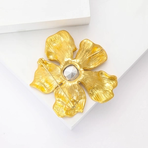 Detailansicht der mattgoldenen Blumenbrosche mit Strassstein auf geometrischem Sockel
